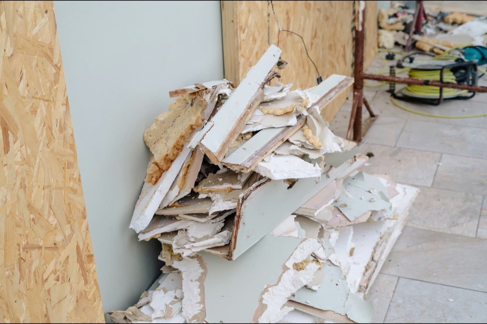 Un tas de panneaux de gypse arrachés, empilés contre un mur d'OSB, sur le plancher d'un logement en démolition.